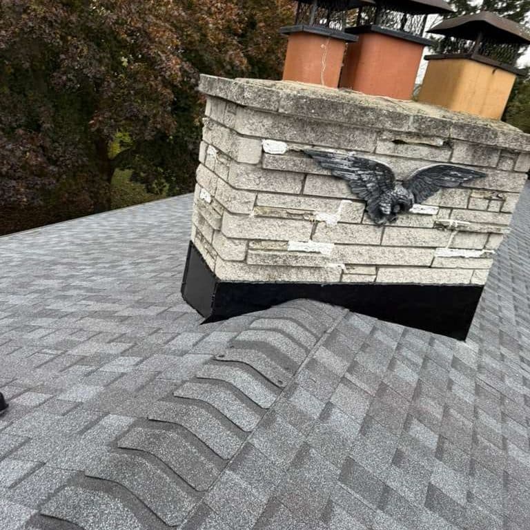 Chimenea de piedra con flashing negro nuevo y un águila de hierro, terminada con tejas grises
