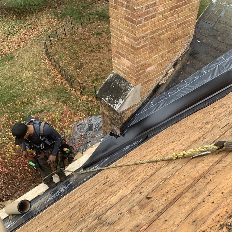 Providence Roofing crew member in a harness detailing ice and water shield around a brick chimney